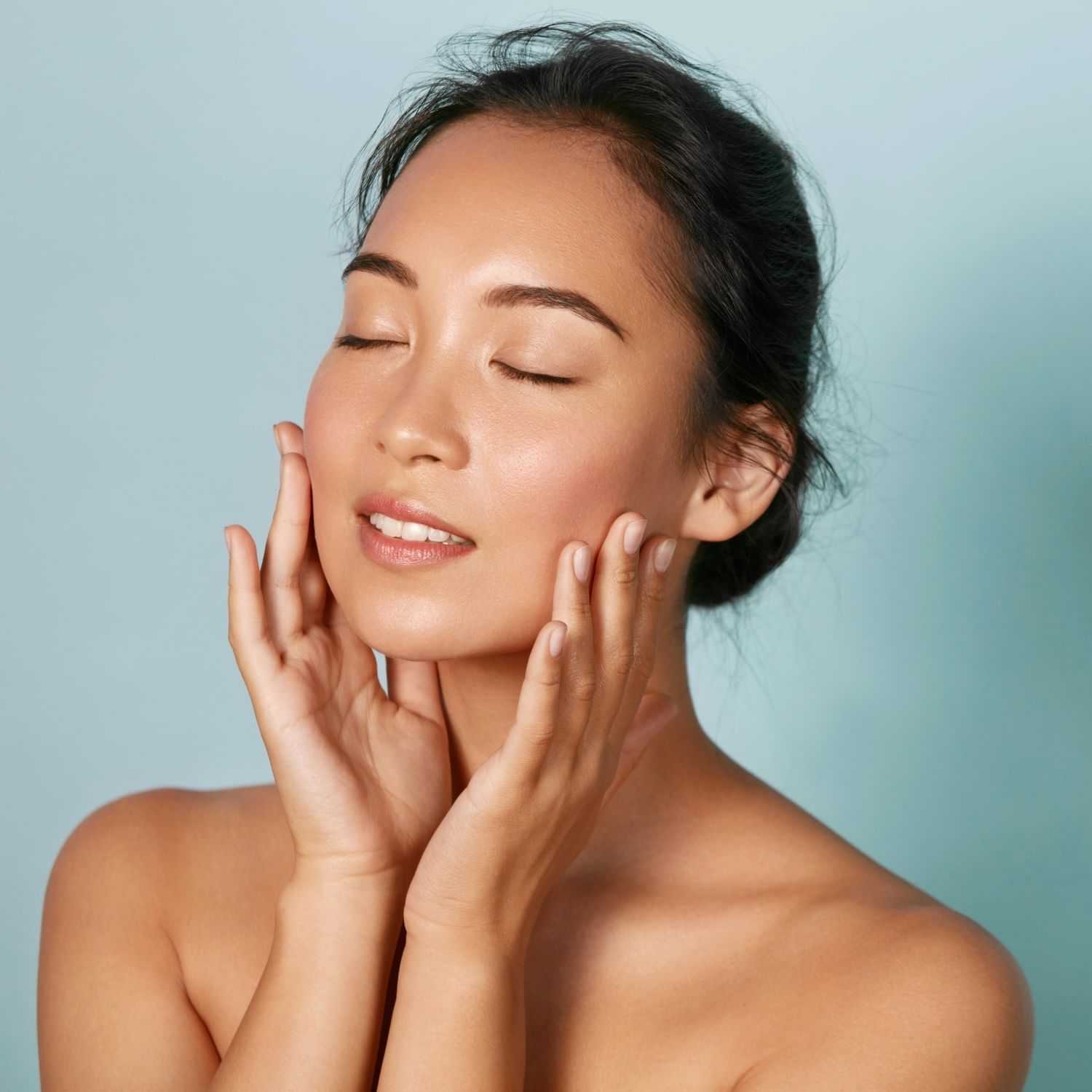 Woman with closed eyes gently touching her face, showcasing healthy and glowing skin.