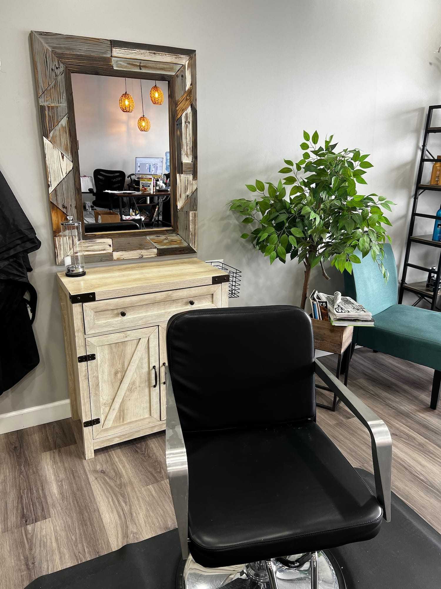 Modern salon chair facing large mirror, with hanging lights, plants, and stylish decor.