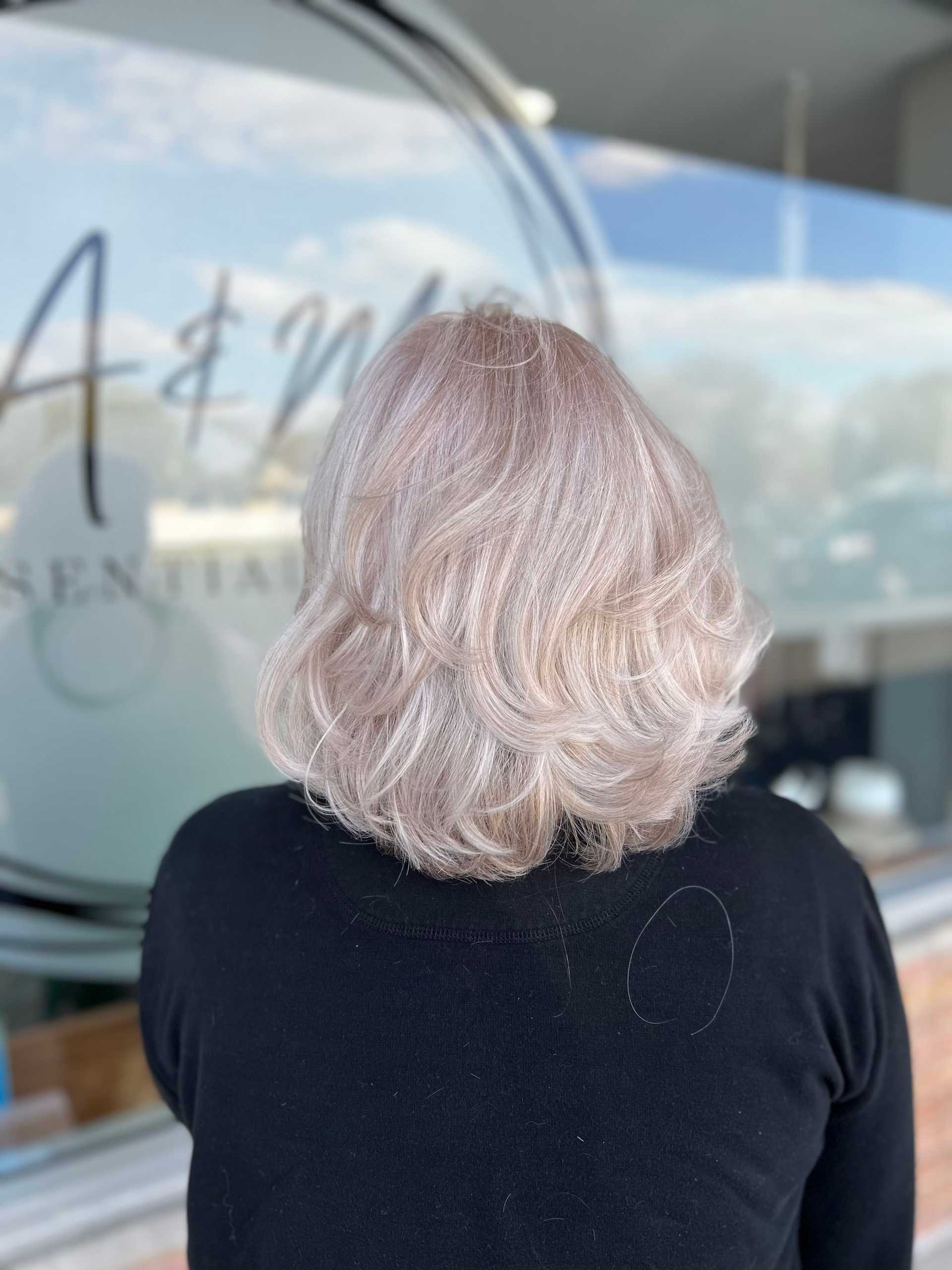 Short blonde hair with soft waves, viewed from the back, against a window backdrop.